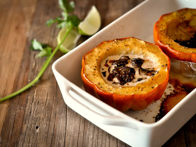 Baked acorn squash halves filled with creamy mushroom sauce in a white baking dish, with lime wedges beside