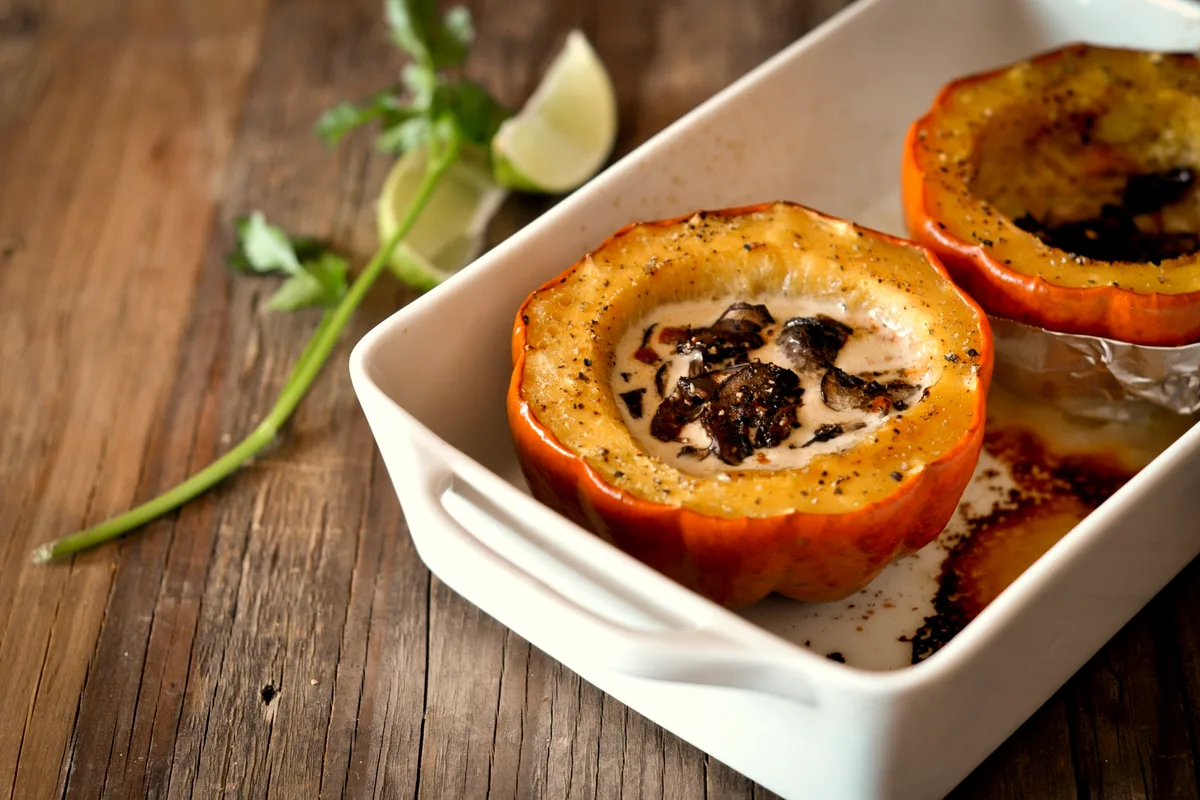 Baked acorn squash halves filled with creamy mushroom sauce in a white baking dish, with lime wedges beside
