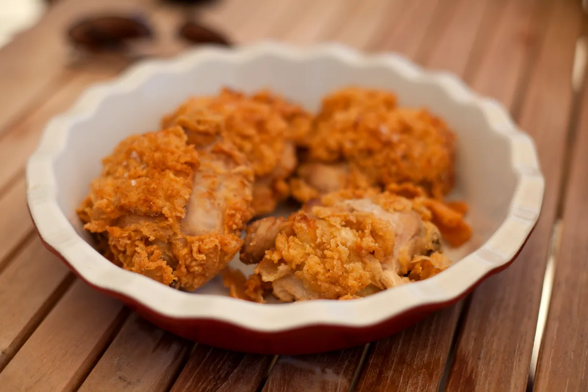 A fluted bowl of golden fried chicken pieces with a craggy, well-seasoned crust on a wooden table