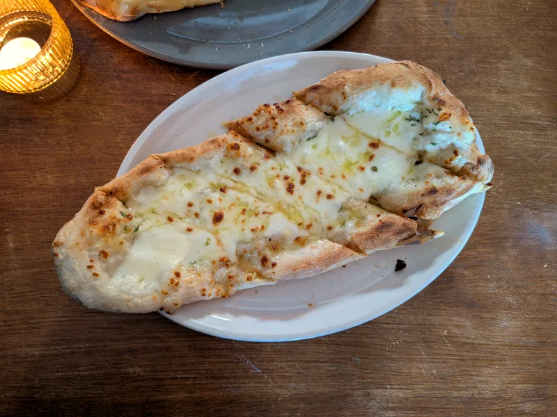 A long cheesy garlic bread with bubbling mozzarella and golden browned spots on a white oval plate on a wooden table
