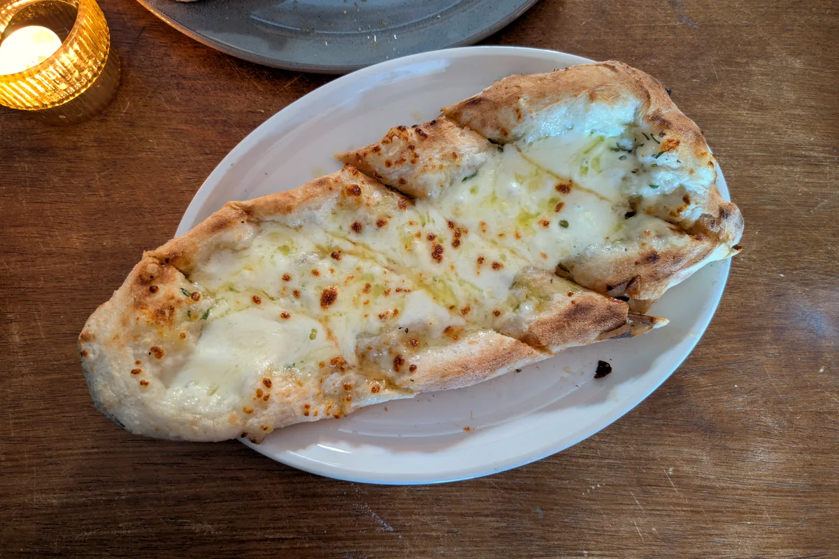 A long cheesy garlic bread with bubbling mozzarella and golden browned spots on a white oval plate on a wooden table