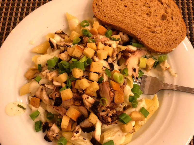 A plate of creamy pasta with grilled chicken, mushrooms, green onions and croutons