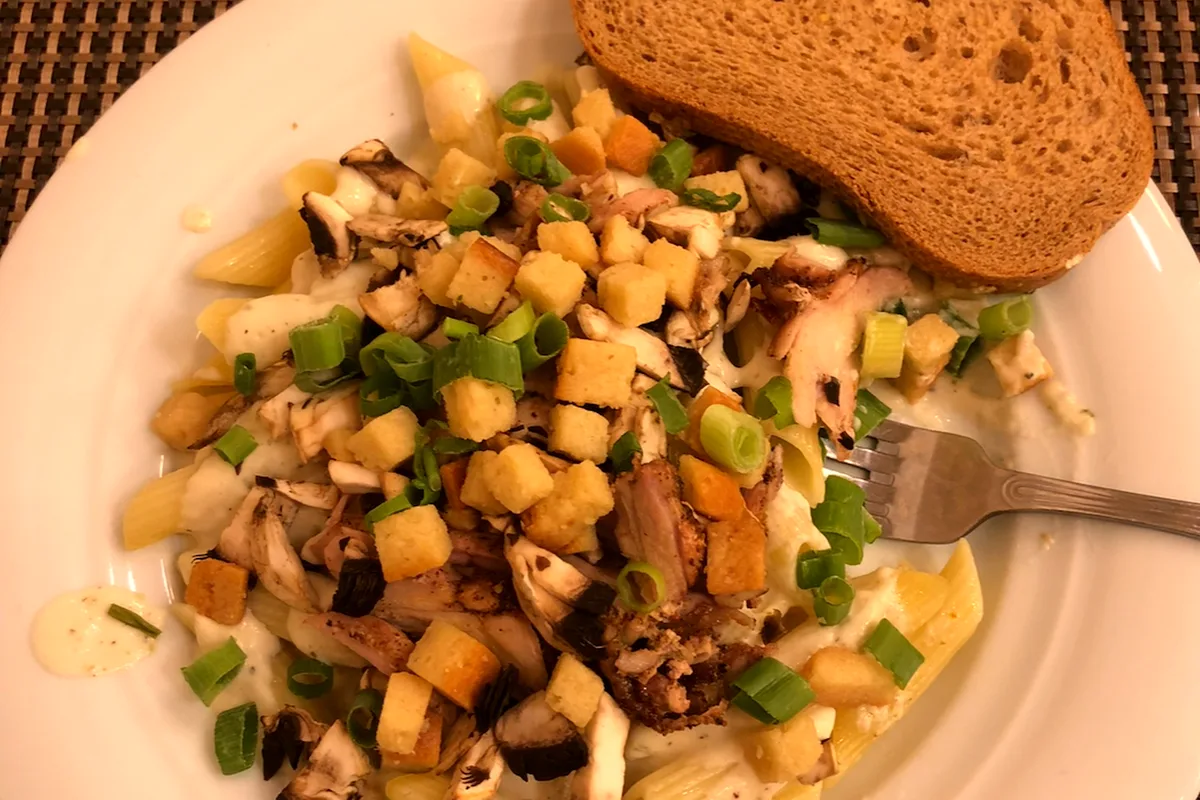 A plate of creamy pasta with grilled chicken, mushrooms, green onions and croutons