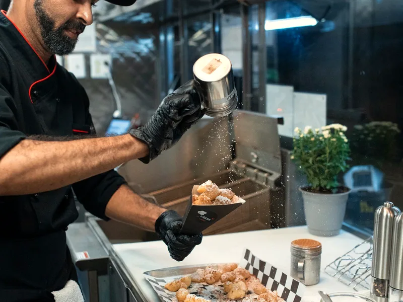 Freshly fried apple fritters being dusted with powdered sugar