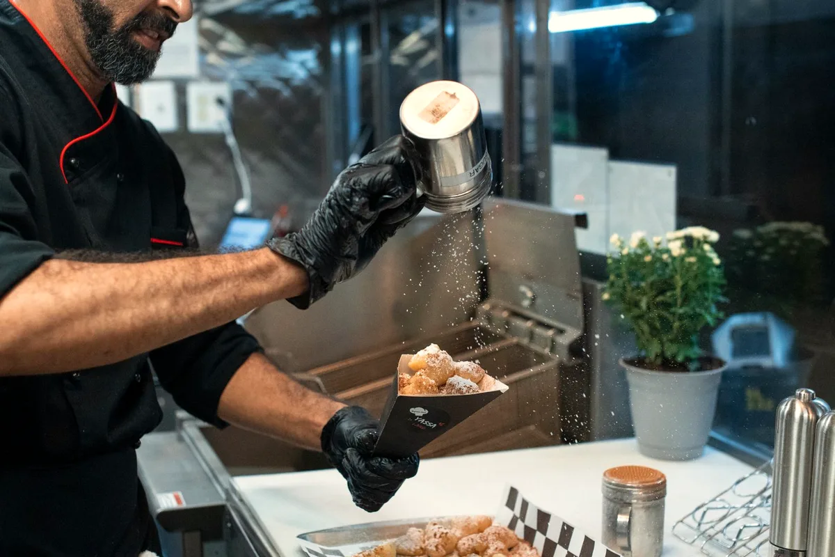 Freshly fried apple fritters being dusted with powdered sugar