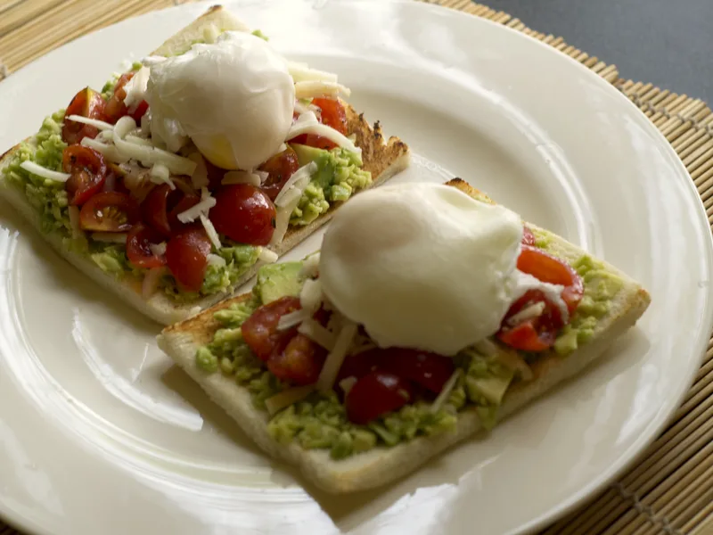 Easy avocado toast with eggs — two toasts with smashed avocado, cherry tomatoes and poached eggs on a white plate