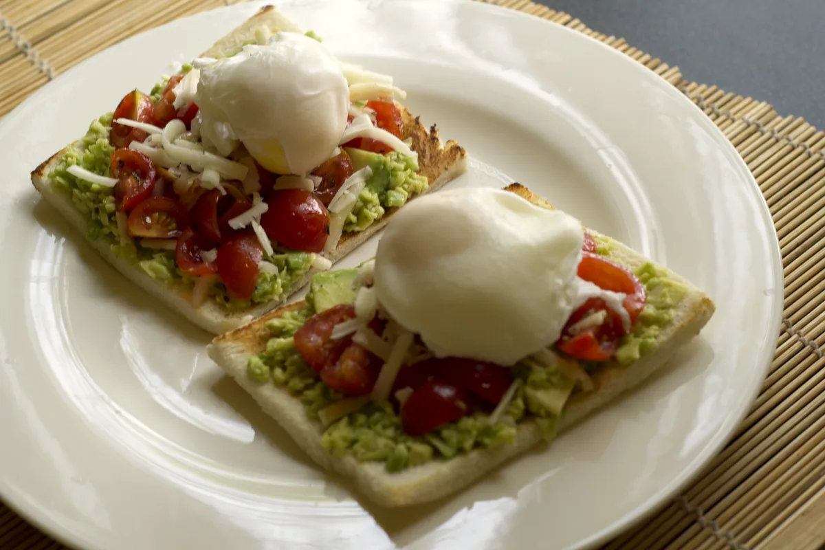 Easy avocado toast with eggs — two toasts with smashed avocado, cherry tomatoes and poached eggs on a white plate