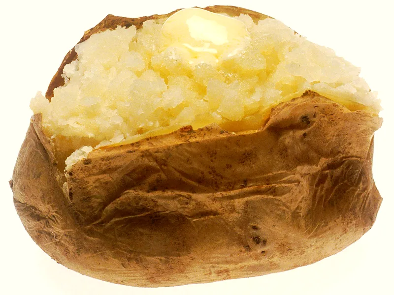 Split baked potato with crisp russet skin, fluffy white flesh and a melting pat of butter on top
