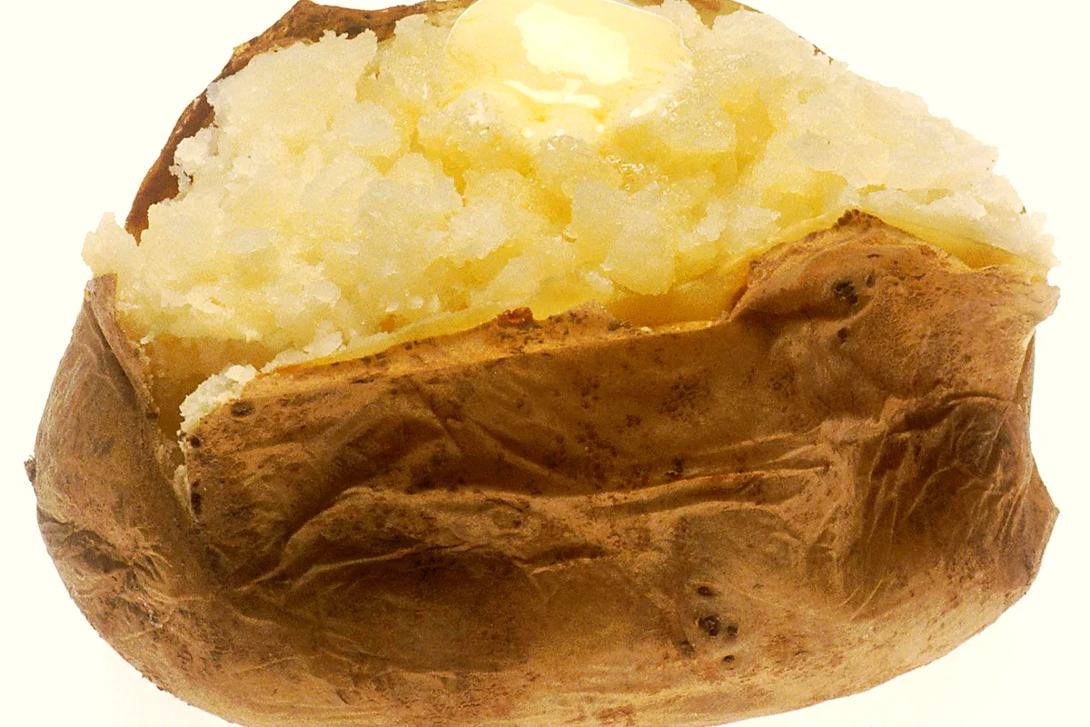 Split baked potato with crisp russet skin, fluffy white flesh and a melting pat of butter on top