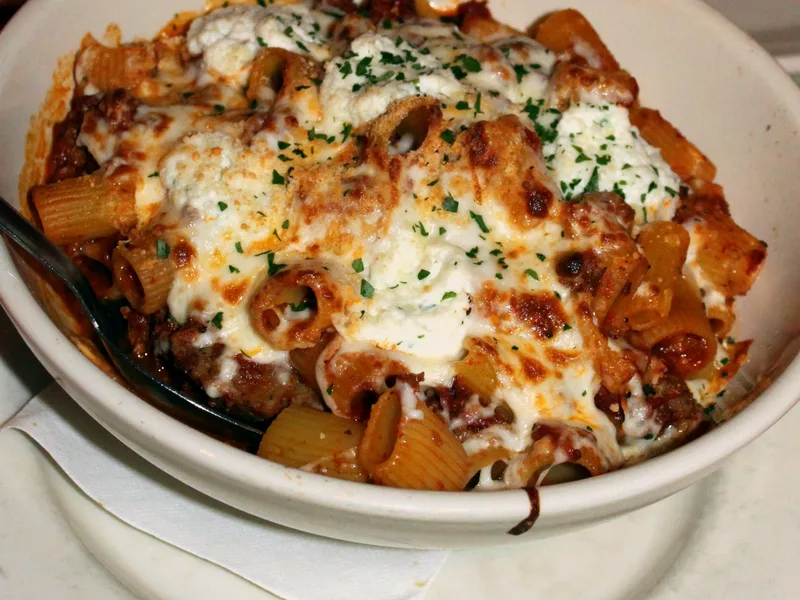 Bowl of easy baked ziti with ricotta dollops, melted mozzarella and tomato meat sauce, sprinkled with parsley