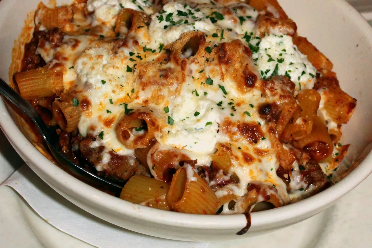 Bowl of easy baked ziti with ricotta dollops, melted mozzarella and tomato meat sauce, sprinkled with parsley