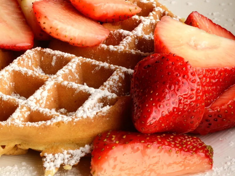 A crisp golden Belgian waffle dusted with powdered sugar and piled with sliced fresh strawberries