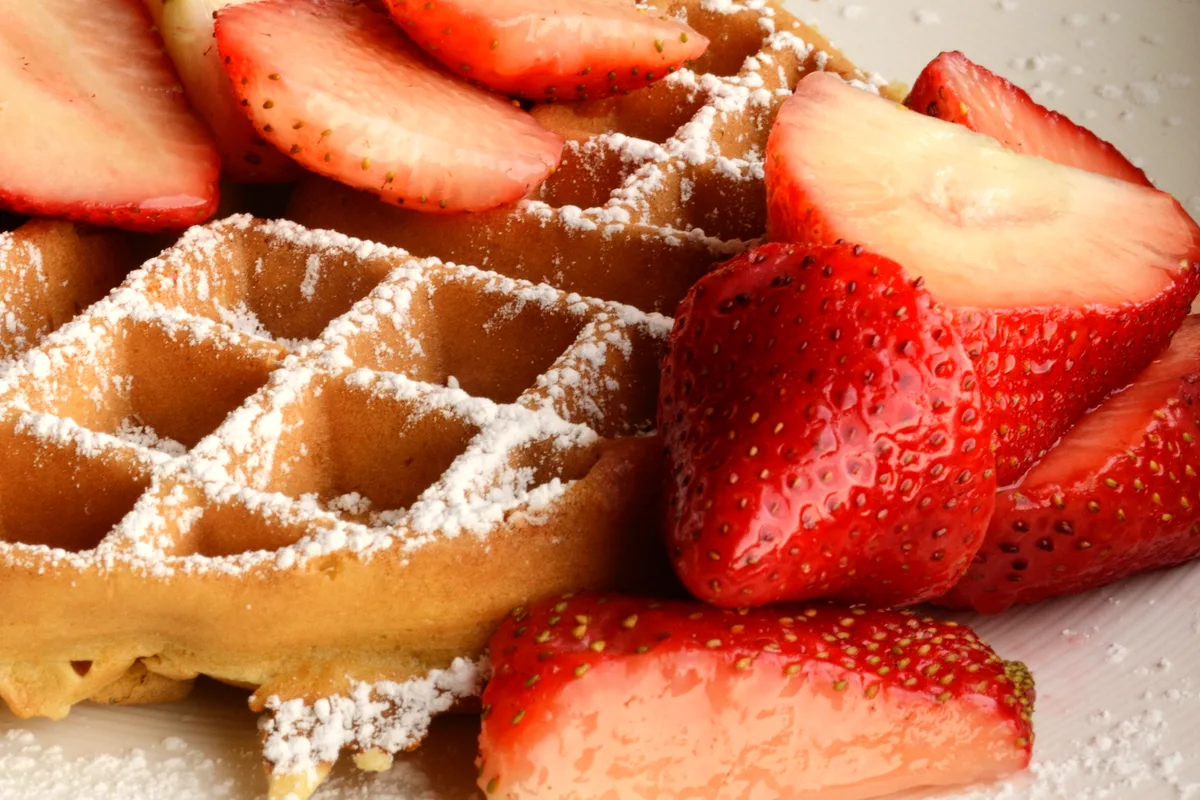 A crisp golden Belgian waffle dusted with powdered sugar and piled with sliced fresh strawberries
