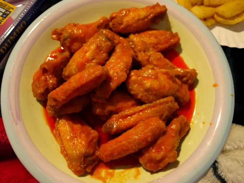 Plate piled with glossy buffalo chicken wings coated in orange-red hot sauce