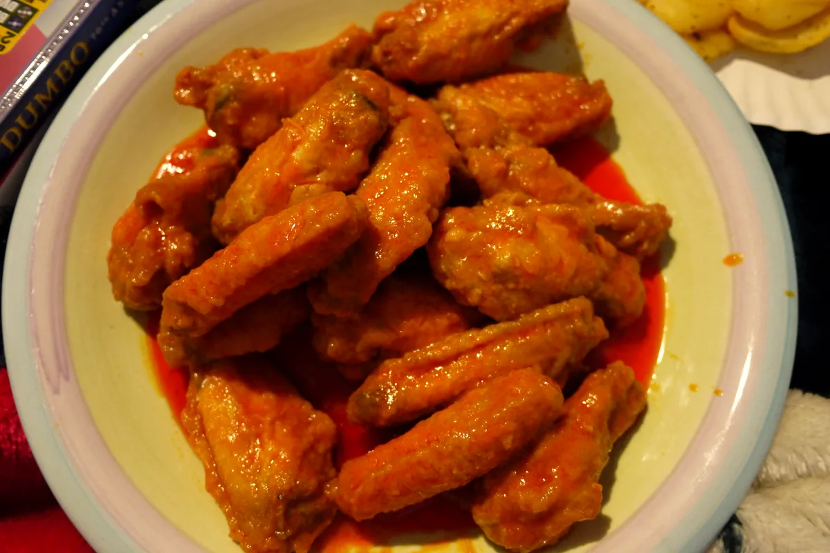 Plate piled with glossy buffalo chicken wings coated in orange-red hot sauce