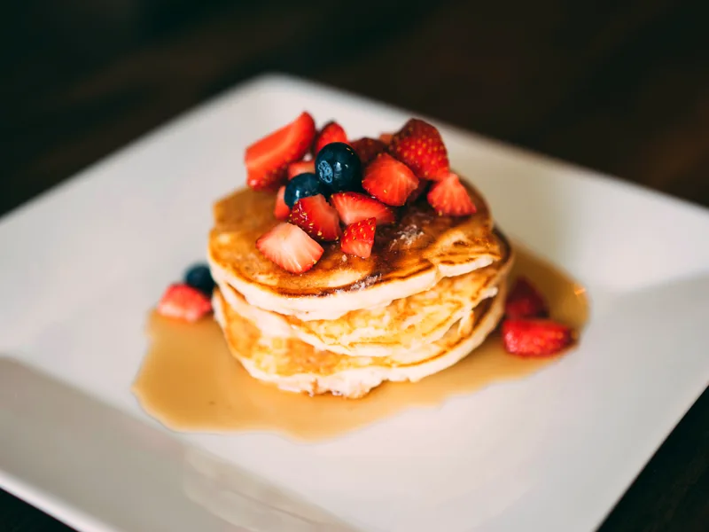 Stack of fluffy buttermilk pancakes topped with strawberries and blueberries with syrup on a white plate