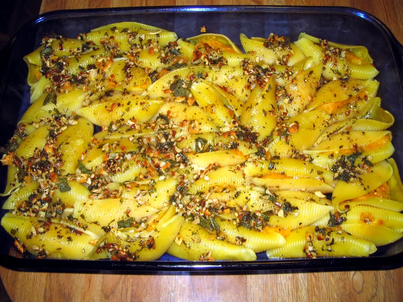 Glass baking dish of butternut squash stuffed shells topped with toasted pecan pieces and crisped sage in brown butter