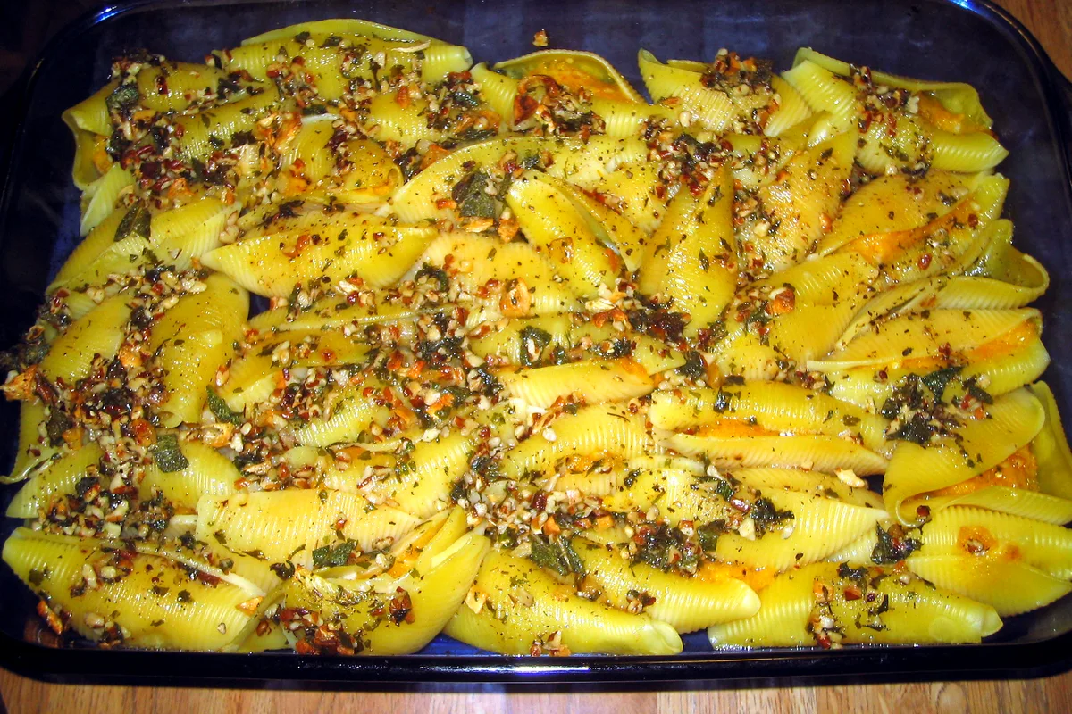 Glass baking dish of butternut squash stuffed shells topped with toasted pecan pieces and crisped sage in brown butter