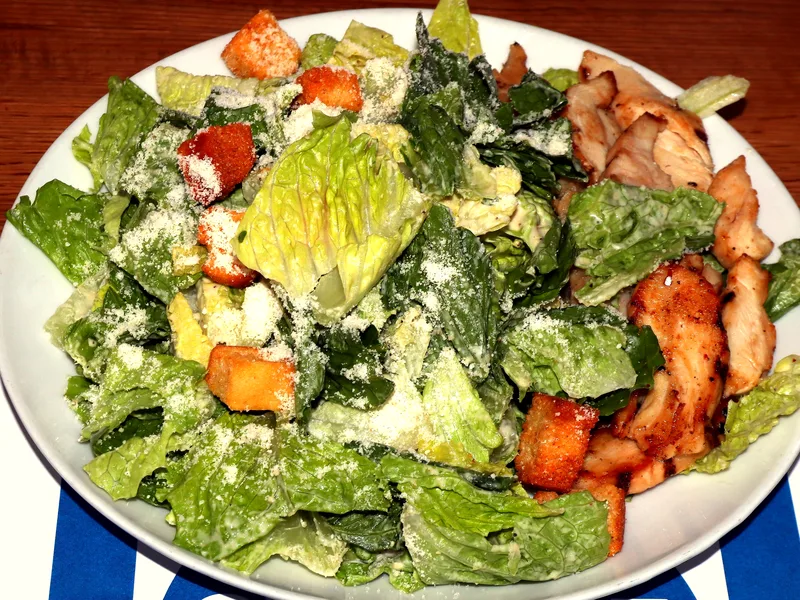 A large plate of Caesar salad with crisp romaine, golden croutons and grated Parmesan, topped with sliced grilled chicken