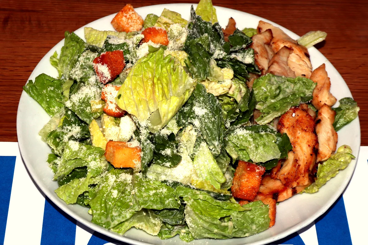 A large plate of Caesar salad with crisp romaine, golden croutons and grated Parmesan, topped with sliced grilled chicken