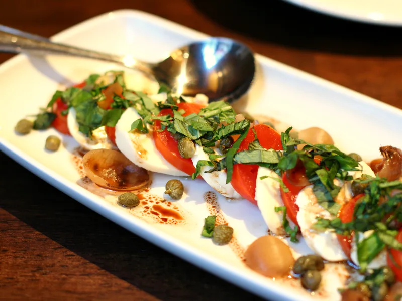 Caprese salad of sliced tomatoes and fresh mozzarella layered with basil leaves on a plate
