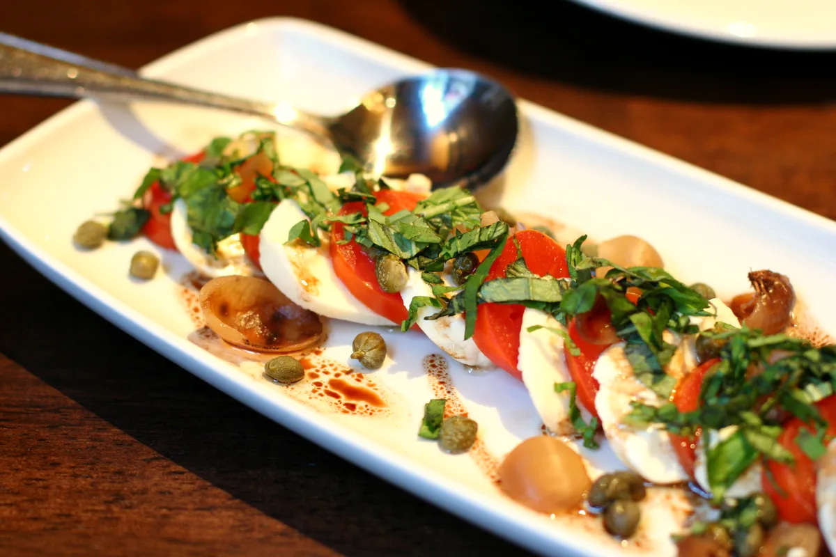 Caprese salad of sliced tomatoes and fresh mozzarella layered with basil leaves on a plate