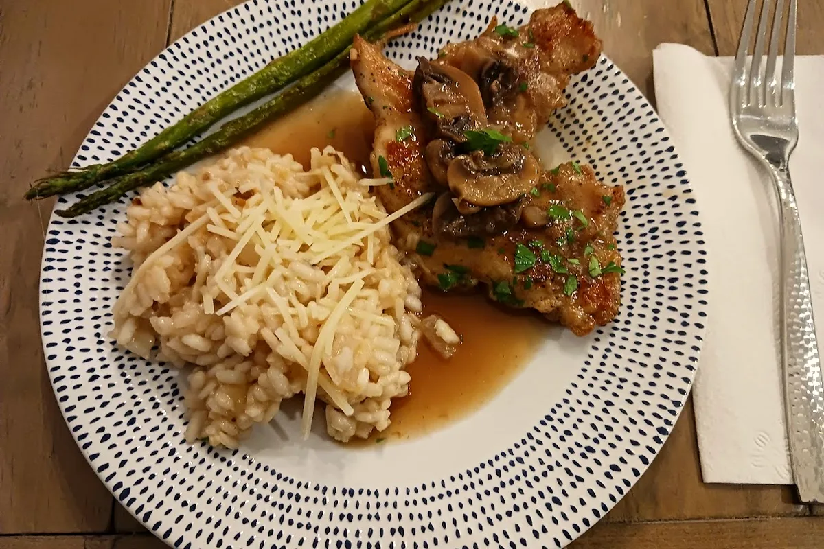Chicken marsala cutlets topped with mushrooms in brown marsala sauce, served with risotto and asparagus