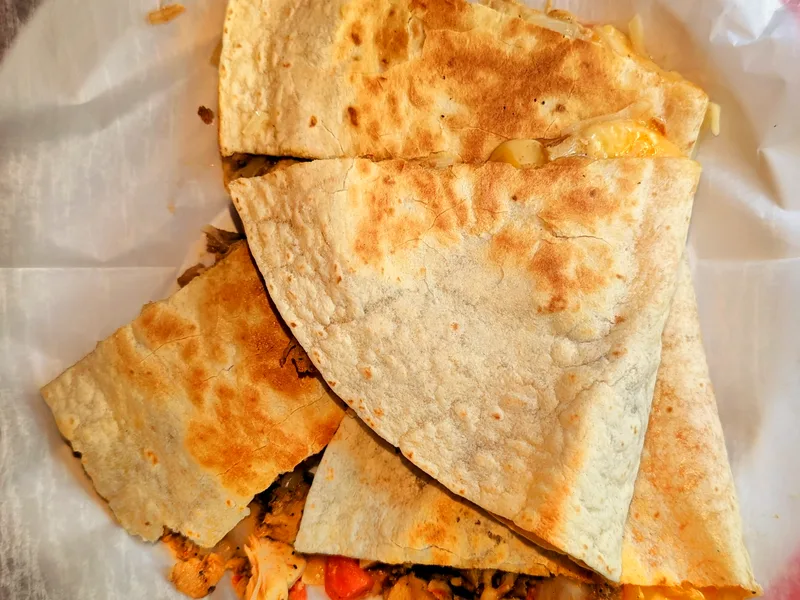 Golden chicken quesadilla wedges stacked on parchment, with melted cheese, peppers and onion spilling from the cut edges