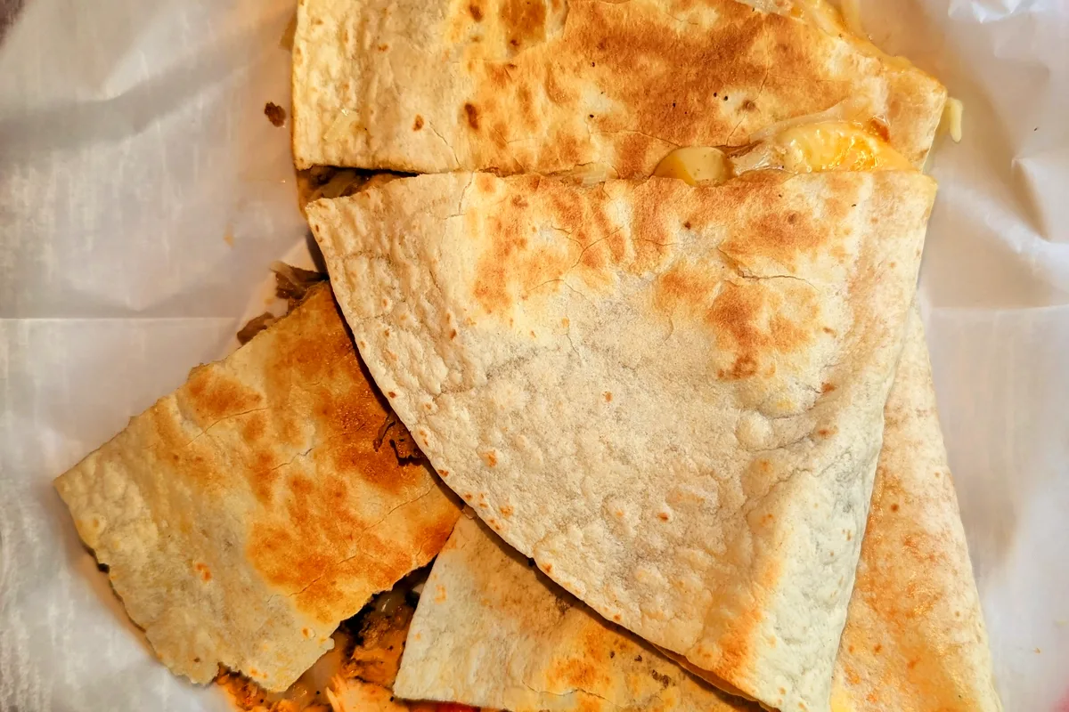 Golden chicken quesadilla wedges stacked on parchment, with melted cheese, peppers and onion spilling from the cut edges