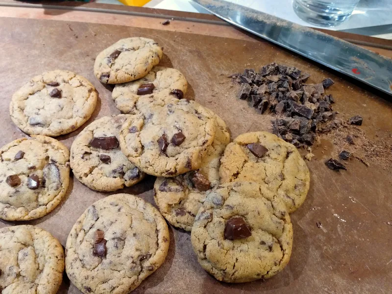 Freshly baked chocolate chip cookies with chocolate chunks cooling on a wooden board next to chopped chocolate