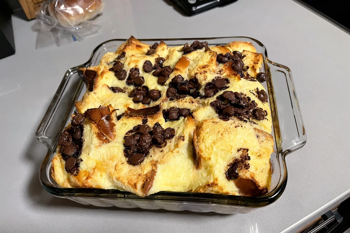 Chocolate chip bread pudding baked golden in a clear glass baking dish, custardy brioche cubes studded with melted chocolate chips