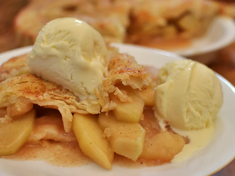 Slice of classic apple pie with tender cinnamon apple filling and flaky crust, served with vanilla ice cream