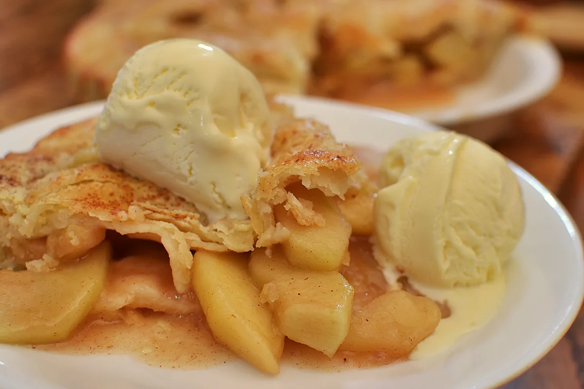 Slice of classic apple pie with tender cinnamon apple filling and flaky crust, served with vanilla ice cream
