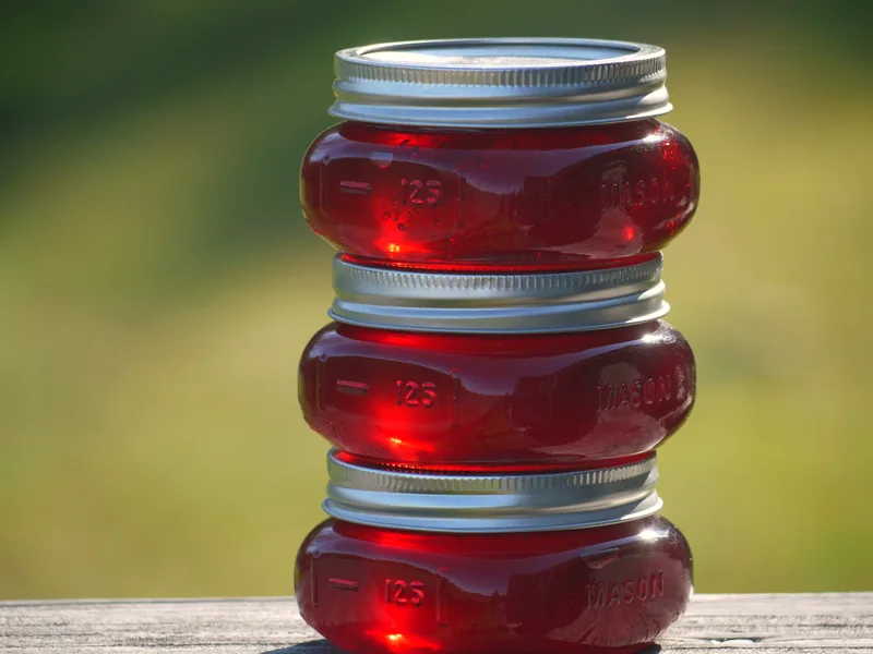 Three small mason jars of clear, jewel-red crab apple jelly stacked outdoors, glowing in sunlight
