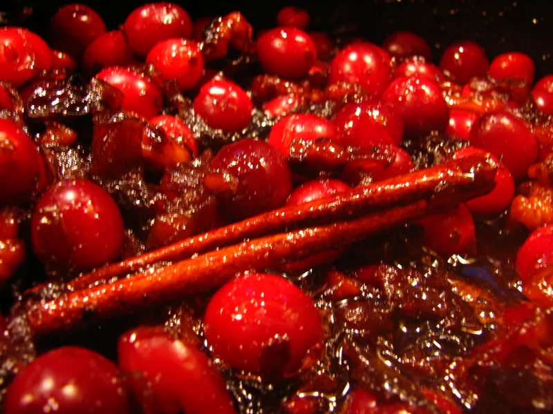 Whole glossy cranberries simmering in dark spiced chutney with a cinnamon stick in the pot