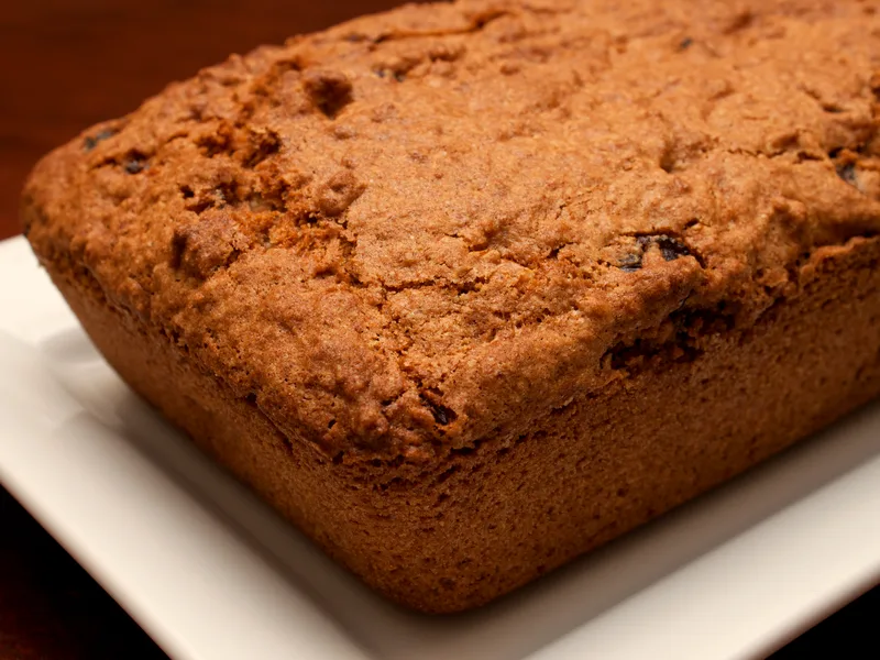 Golden-brown cranberry orange nut loaf on a white plate, cranberries showing in the crust