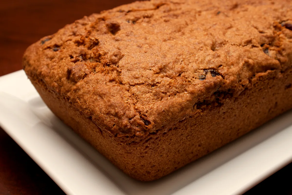 Golden-brown cranberry orange nut loaf on a white plate, cranberries showing in the crust