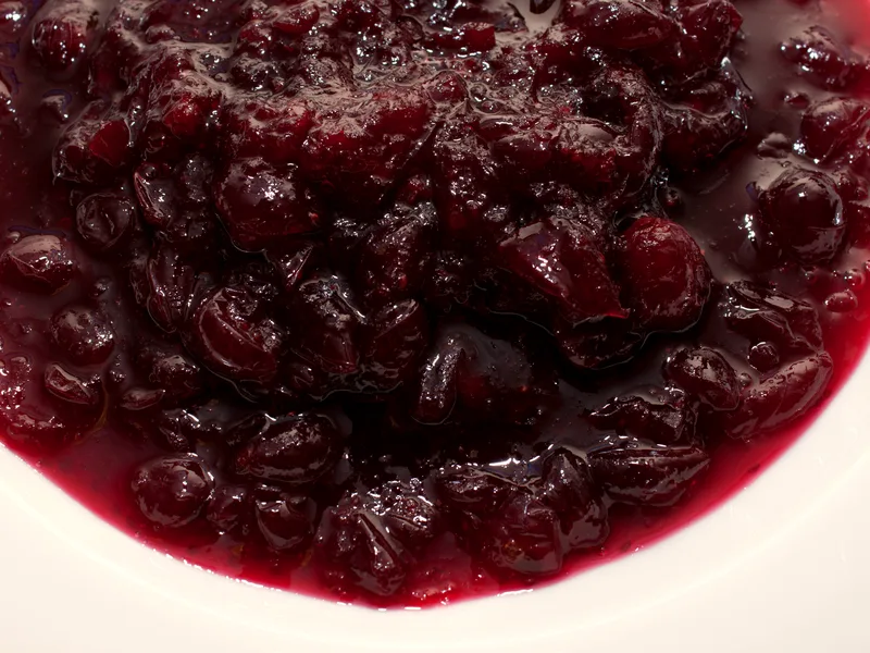 Close-up of whole berry cranberry sauce in a white bowl, deep red and glossy, with whole softened cranberries visible throughout