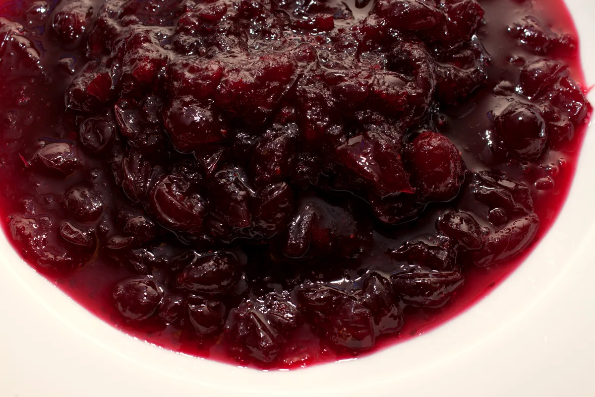 Close-up of whole berry cranberry sauce in a white bowl, deep red and glossy, with whole softened cranberries visible throughout