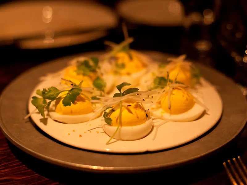 Deviled eggs with bright yellow piped filling, parsley and a fine shaved garnish on a white plate