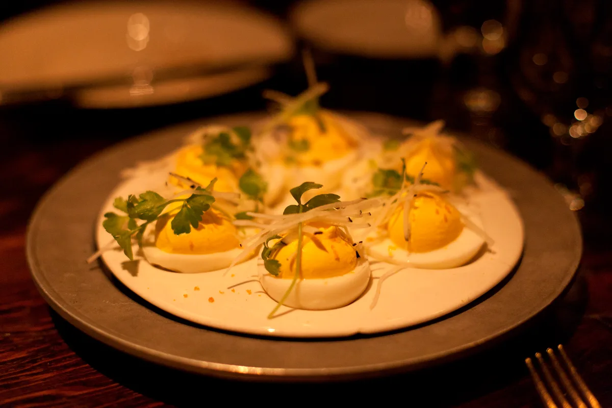 Deviled eggs with bright yellow piped filling, parsley and a fine shaved garnish on a white plate