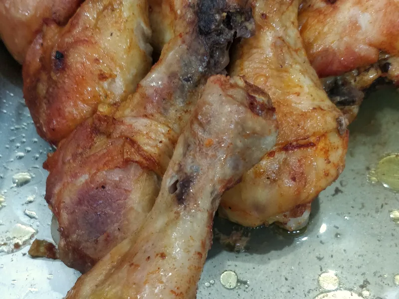 A pile of deeply golden roasted chicken drumsticks with crisp, well-browned skin in a steel tray