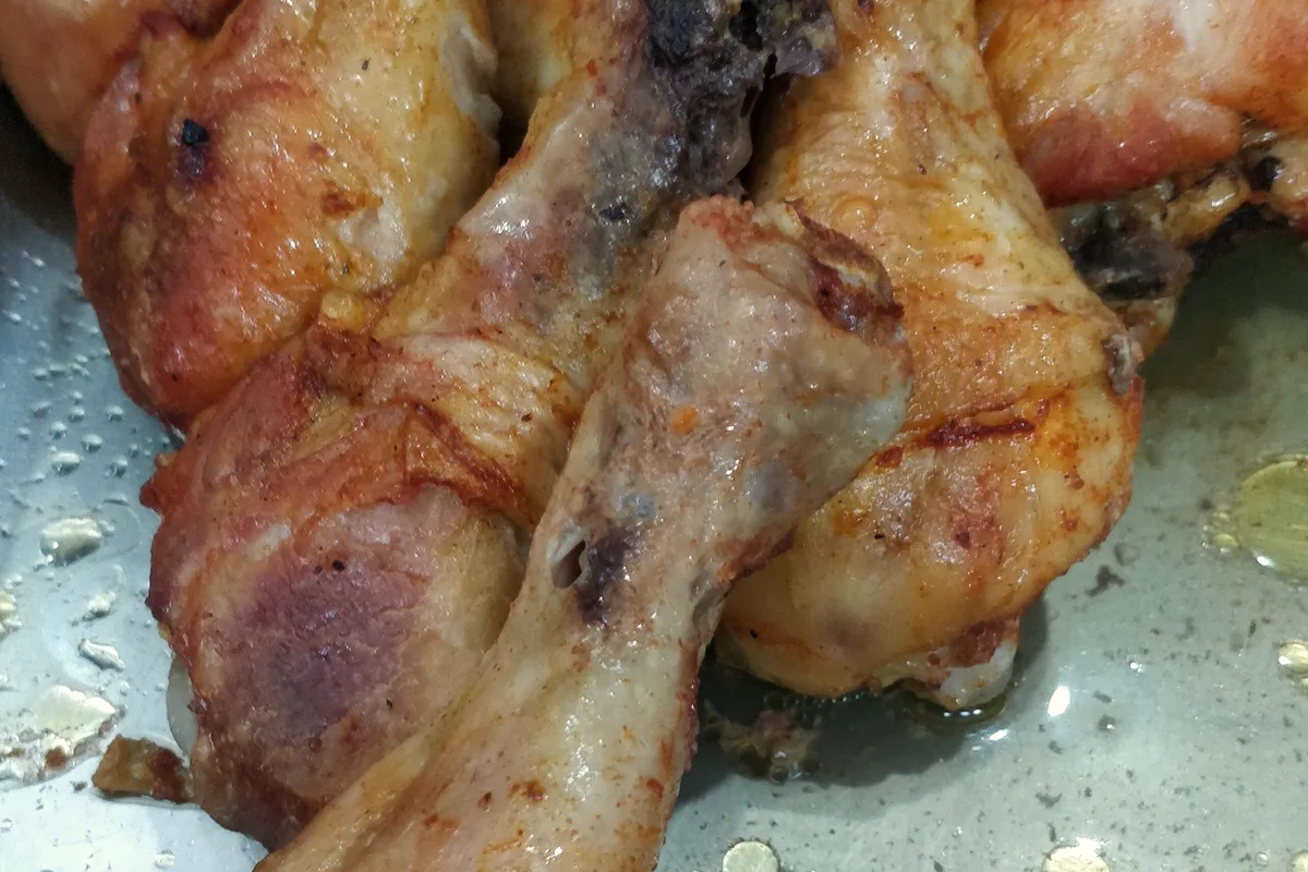 A pile of deeply golden roasted chicken drumsticks with crisp, well-browned skin in a steel tray