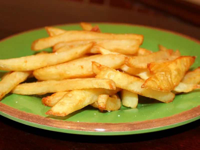 Pile of golden crispy french fries lightly salted on a green plate