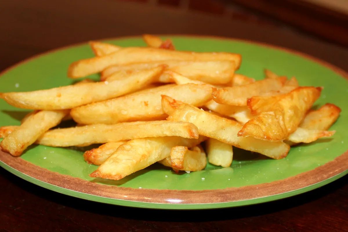 Pile of golden crispy french fries lightly salted on a green plate