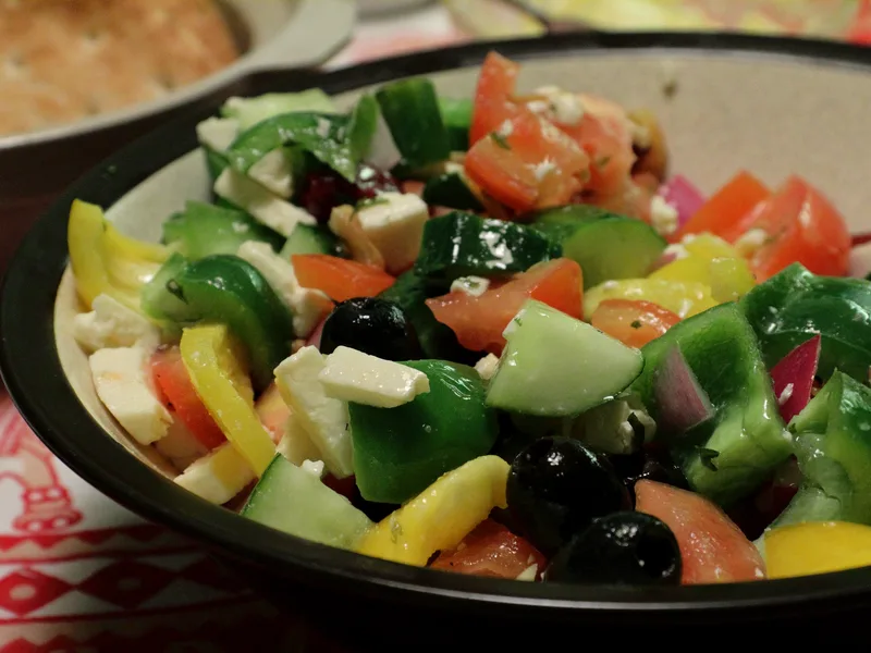 A bowl of chunky Greek salad with tomatoes, cucumber, green and yellow peppers, black olives, red onion and cubes of feta cheese