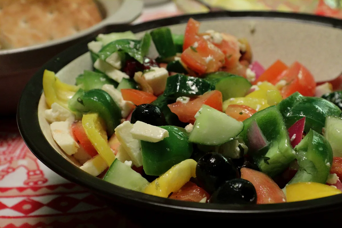 A bowl of chunky Greek salad with tomatoes, cucumber, green and yellow peppers, black olives, red onion and cubes of feta cheese