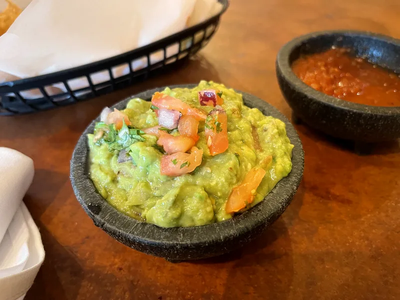 Easy homemade guacamole in a stone bowl topped with diced tomato, onion and cilantro, with salsa and tortilla chips beside it