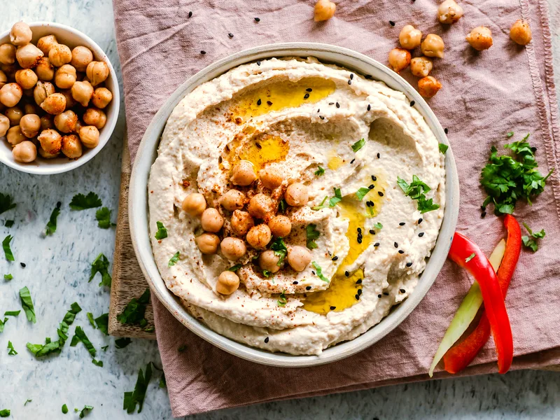 A bowl of smooth hummus swirled with pools of olive oil and topped with whole chickpeas, paprika and fresh herbs