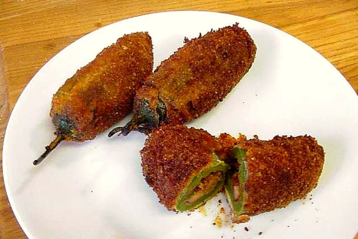 Three whole baked jalapeno poppers with a deep golden breadcrumb crust on a white plate, one cut open to show the green pepper wall and creamy filling inside